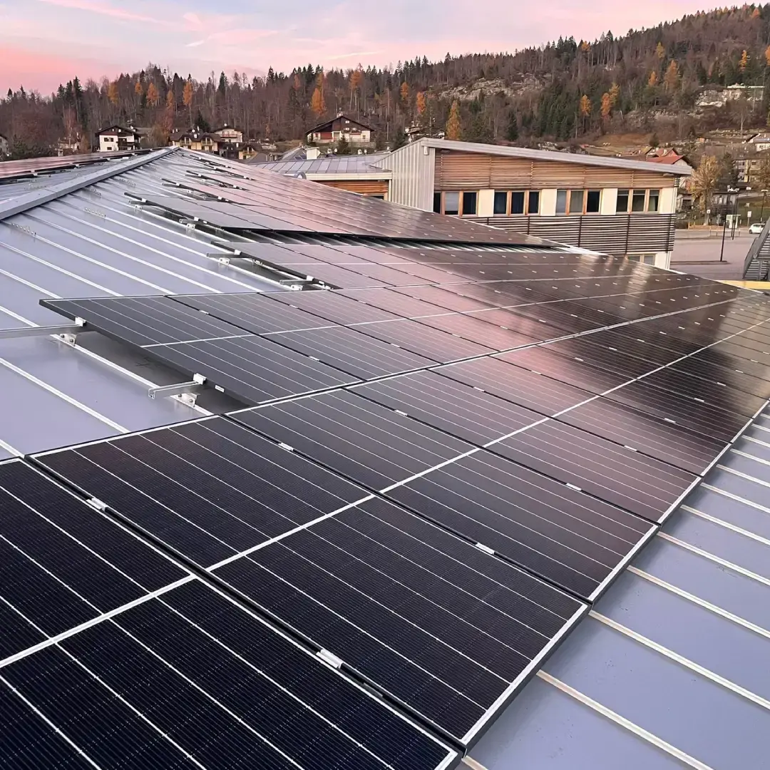 Pannelli fotovoltaici su tetto di edificio pubblico in contesto montano trentino al tramonto