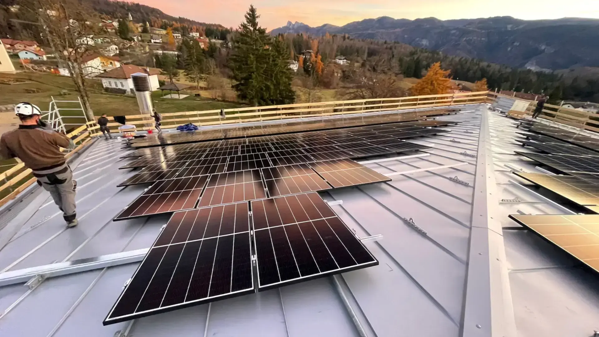 Tecnici che installano pannelli fotovoltaici su tetto in contesto montano trentino al tramonto