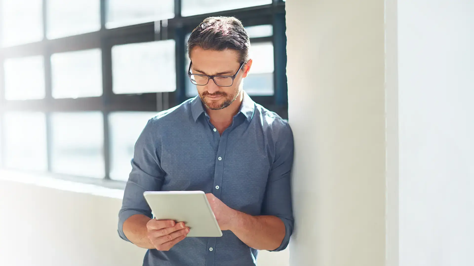 Professionista con occhiali che consulta tablet in ufficio luminoso