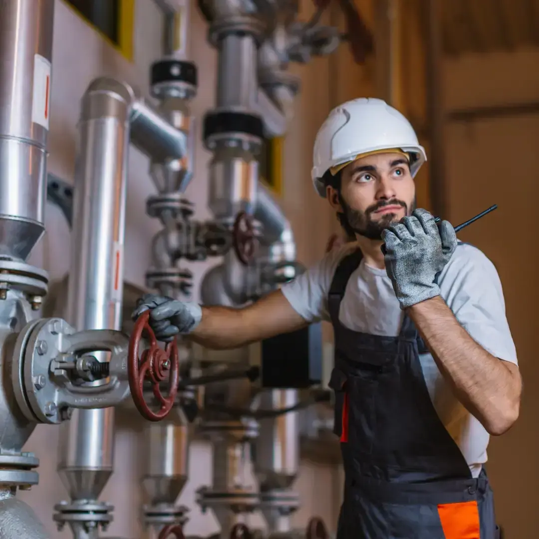 Tecnico con elmetto che manovra valvola su impianto di tubature durante manutenzione